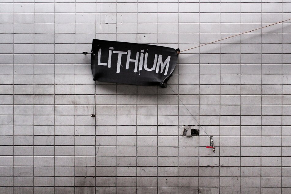 A grey cloth banner with the word “LITHIUM” written in white, hanging from a string on a white tiled wall.