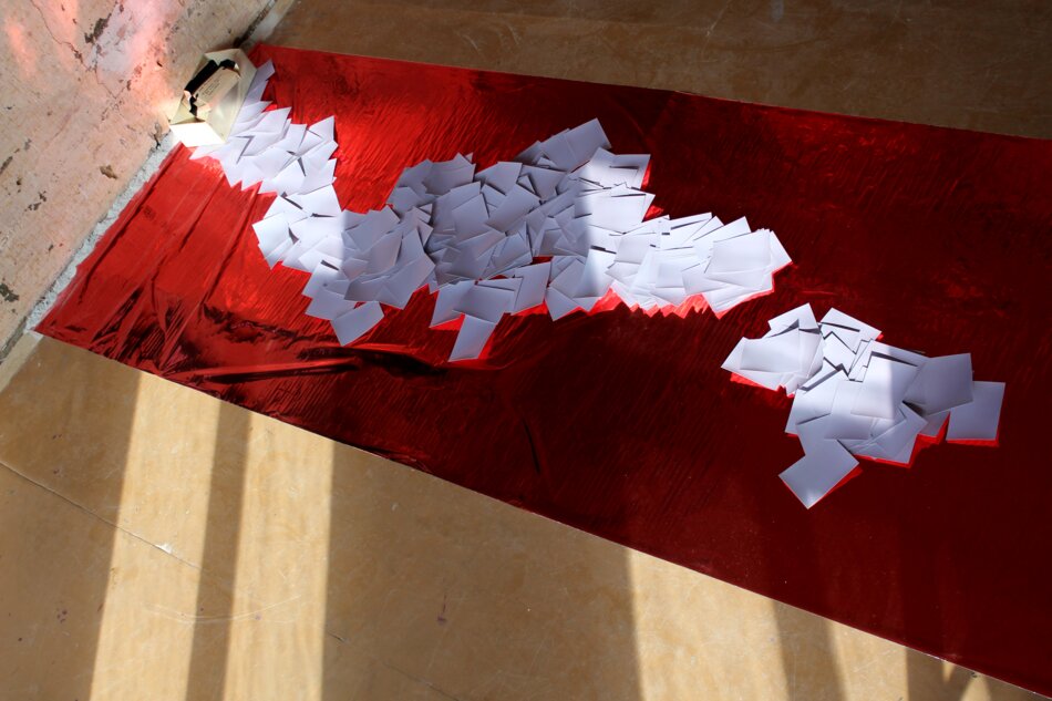 A red surface covered with white paper scraps arranged in a winding, snake-like pattern.