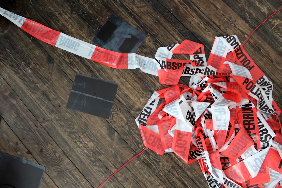 Red and white police caution tape is scattered across a wooden floor, with three bird X-rays lying nearby.